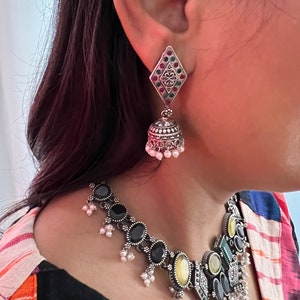 May include: Silver-toned necklace and earring set. The necklace features black and yellow oval stones, with small white pearl accents. The earrings have a diamond-shaped top with red, green, and silver accents, and a bell-shaped bottom with white pearl dangles.