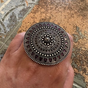 Può includere: Un grande anello d'argento con un design circolare che presenta un motivo a mandala con accenti viola.