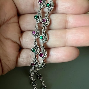 Pode incluir: Um bracelete de corrente de prata com pedras preciosas verdes e rosa. A corrente é feita de pequenos elos intrincados e apresenta um design delicado.