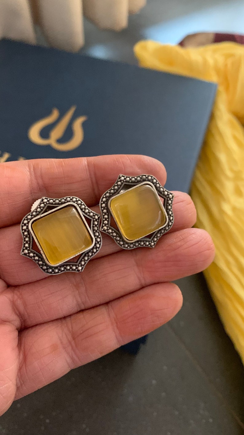 May include: A pair of silver earrings with a yellow gemstone in the center of each earring. The earrings have a decorative, ornate design.