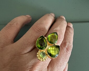 Può includere: Un anello d'oro con un gruppo di cinque gocce di pietre preziose verdi. L'anello è incastonato con una pietra preziosa verde più piccola al centro.