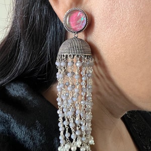 May include: Silver dangle earrings with a gray and white beaded tassel and a round iridescent pink and blue stone.