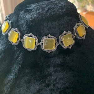 May include: A silver choker necklace with a geometric design and yellow square-shaped stones.