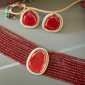 May include: A red gemstone necklace with a multi-strand design. The necklace features a large, red gemstone pendant and two smaller red gemstone earrings.