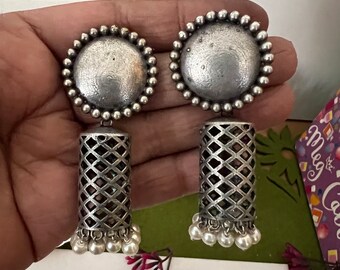 May include: A pair of silver earrings with a round, textured top and a dangling, openwork cylinder with white beads at the bottom.