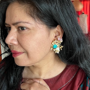 Peut inclure: Une paire de boucles d'oreilles dorées avec une pierre turquoise et des accents de perles blanches. Les boucles d'oreilles ont la forme d'un motif floral.