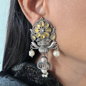 May include: Silver earrings with a floral design and yellow and white stones. The earrings have a bell-shaped dangle with pearl accents.