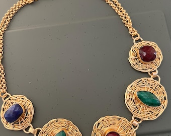 Puede incluir: Un collar de oro con cuatro colgantes circulares, cada uno con una piedra preciosa de color diferente. Las piedras preciosas son roja, verde, azul y verde. El collar está hecho de una cadena delicada.