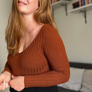 Könnte beinhalten: Eine Frau mit langen, roten Haaren trägt einen rostigen, gerippten Strickpullover mit V-Ausschnitt.