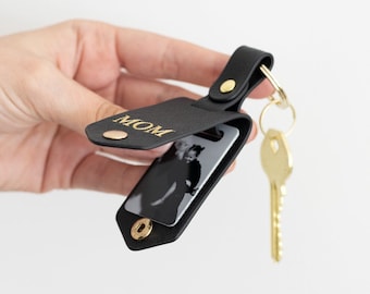 May include: Black leather keychain with a photo holder that opens to reveal a photo. The keychain has a gold ring and a gold key attached. The photo holder is engraved with the word "MOM".