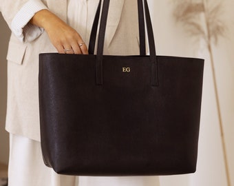 Può includere: Una borsa tote in pelle nera con dettagli dorati e le iniziali "EG" incise sul davanti.