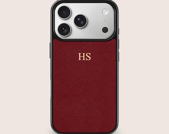 May include: A burgundy phone case with a black border and a silver camera section. The case features the gold initials "HS" and is designed to protect the phone. The case is made of a textured material.
