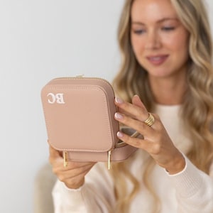 May include: A blush pink jewellery box with a gold zipper and gold accents. The box is monogrammed with the initials "BC".