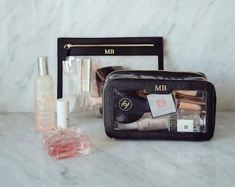 May include: Two black clear makeup bags with gold zippers. The larger bag has the initials "MB" on the front and is filled with various makeup and beauty products. The smaller bag has the initials "MB" on the front and is empty.
