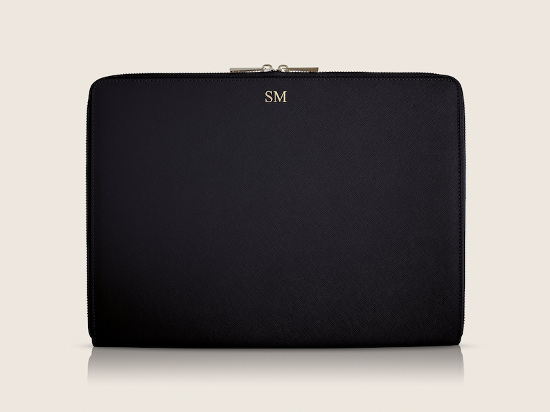 Pu&ograve; includere: Custodia per laptop nera con chiusura a zip e le iniziali "SM" in rilievo sul davanti.
