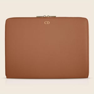 Pu&ograve; includere: Una custodia per laptop in pelle marrone con chiusura a zip e le iniziali "CD" in rilievo sul davanti.