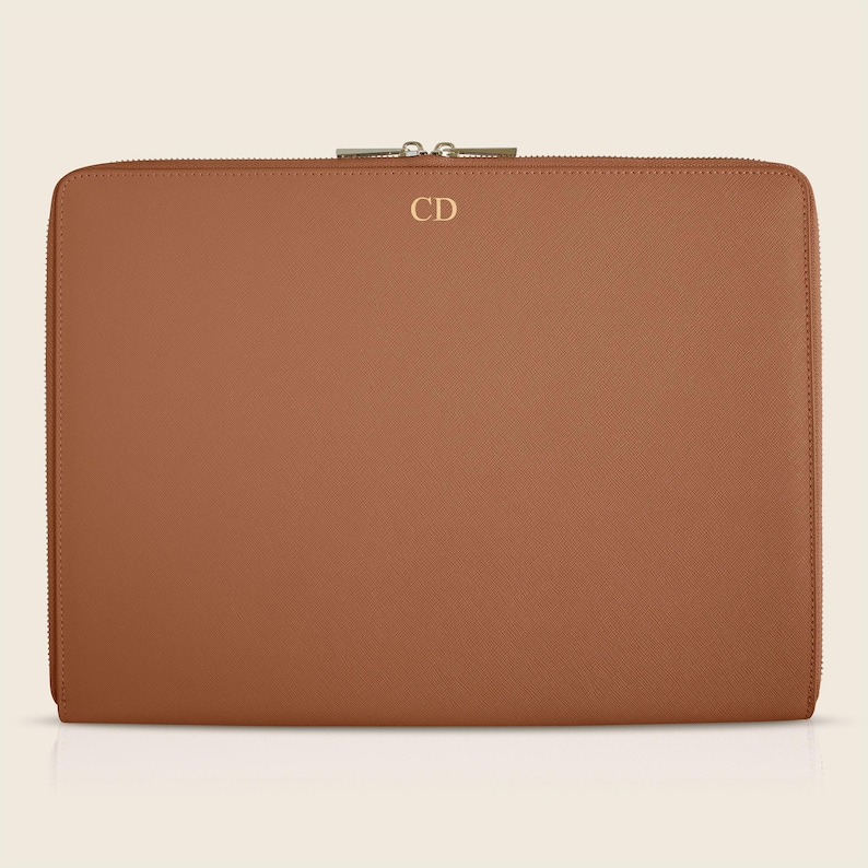 Pu&ograve; includere: Una custodia per laptop in pelle marrone con chiusura a zip e le iniziali "CD" in rilievo sul davanti.