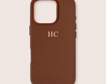 May include: A brown leather phone case with a textured surface. The case has a gold-colored camera ring and the gold initials "HC" are centered on the front. The case has a rectangular shape with rounded corners.