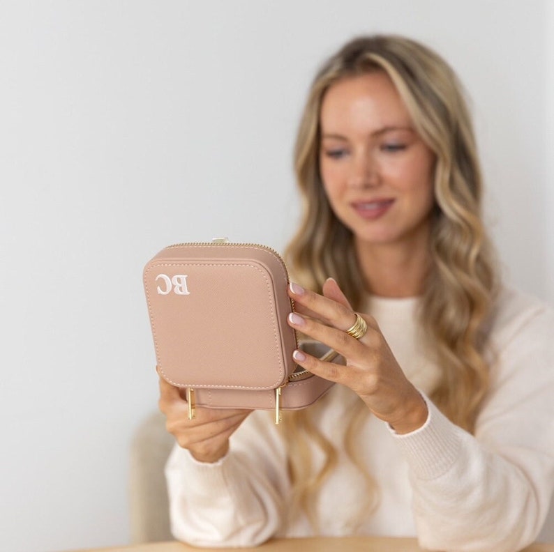 May include: A blush pink jewellery box with a gold zipper and gold accents. The box is monogrammed with the initials "BC".