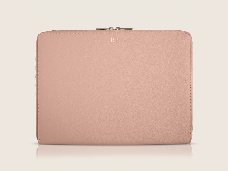 Pu&ograve; includere: Una custodia per laptop rosa cipria con chiusura a zip e le iniziali "RP" in rilievo dorato.