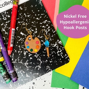 May include: A pair of earrings featuring a paintbrush and a paint palette. The paint palette is brown with colorful paint dots. The earrings are nickel free and hypoallergenic.