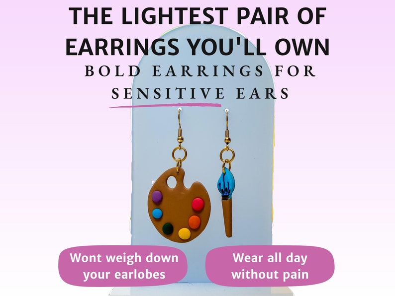 May include: A pair of lightweight earrings featuring a brown paint palette and a blue paintbrush charm. The earrings are advertised as being comfortable for sensitive ears. The text "The lightest pair of earrings you'll own" and "Bold earrings for sensitive ears" is displayed above the earrings. The text "Wont weigh down your earlobes" and "Wear all day without pain" is displayed below the earrings.