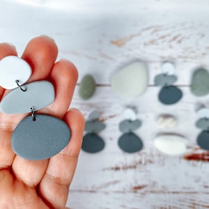 May include: A pair of grey and white statement earrings made of polymer clay. The earrings are shaped like pebbles and are stacked on top of each other.