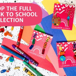 May include: Three cards with colorful back to school themed earrings. Each card has the text "LAUREN LIKES" and features a different set of earrings. The earrings are made of polymer clay and feature school supplies like crayons, paintbrushes, and a globe.
