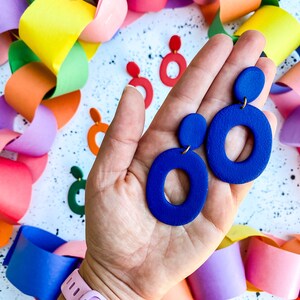 Könnte beinhalten: Ein Paar blaue Statement-Ohrringe mit einem großen Kreisdesign und einem kleineren Kreisakzent. Die Ohrringe sind aus Polymer Clay gefertigt und haben eine matte Oberfläche.