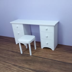 May include: White vanity desk with three drawers on each side and a white stool. The desk and stool are in a room with light brown wood flooring.