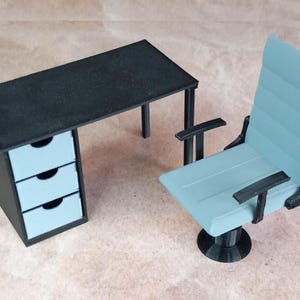 May include: A black desk with three drawers and a light blue office chair with a swivel base. The desk has a black top and black legs. The chair has a light blue seat and back, and black arms and base.