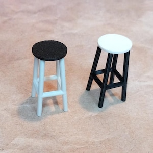 May include: Two wooden stools, one with a black seat and one with a white seat. Both stools have a simple design with four legs and a square frame.
