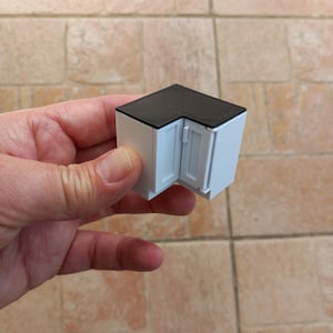Peut inclure: Une armoire d'angle blanche avec un dessus noir. L'armoire a deux portes et est en plastique.