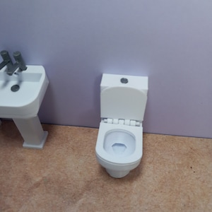 May include: White toilet with a closed lid and a white porcelain bowl. The toilet is in a bathroom setting with a light brown floor.