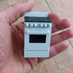 May include: White miniature stove with four black burner elements and a black oven door. The stove has white knobs and a white handle.