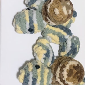 May include: Three crocheted stuffed turtles in a stack. The turtles are made with a mix of green, blue, and yellow yarn. The shells are brown and beige.