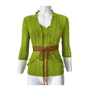 Könnte beinhalten: Ein limegrüner Häkelpullover mit Rüschenkragen und einem braunen Wildledergürtel.