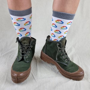 May include: A pair of dark green canvas boots with brown rubber soles and laces. The boots are worn with white socks featuring a repeating pattern of colorful cloud-shaped logos.