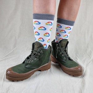 May include: A pair of green canvas ankle boots with brown rubber soles. The boots are worn with white socks featuring a colorful cloud pattern.