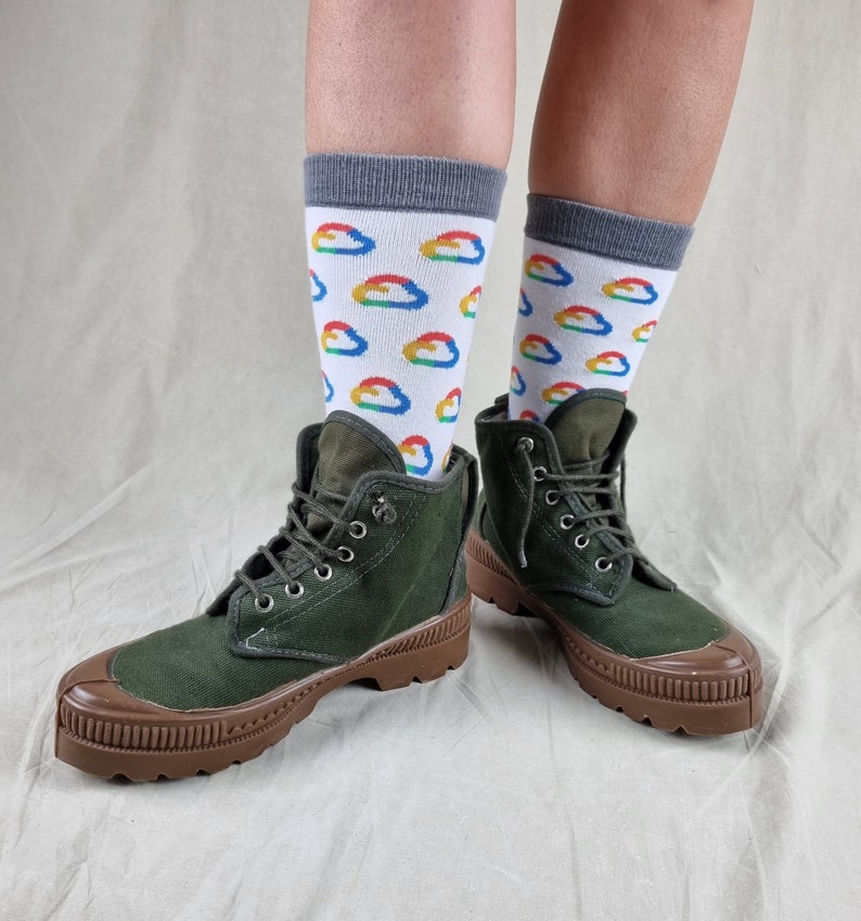 May include: A pair of green canvas ankle boots with brown rubber soles. The boots are worn with white socks featuring a colorful cloud pattern.