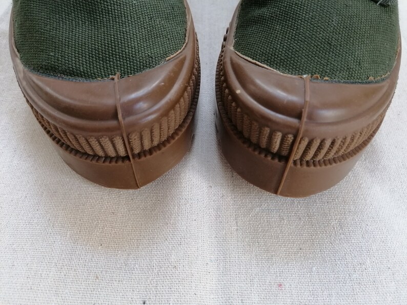May include: A pair of dark green canvas shoes with brown rubber soles. The soles have a textured pattern.