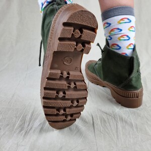 May include: A pair of green canvas boots with brown rubber soles. The boots have a lace-up closure and a textured tread pattern. The text "GELTEX" is visible on the sole of one boot.