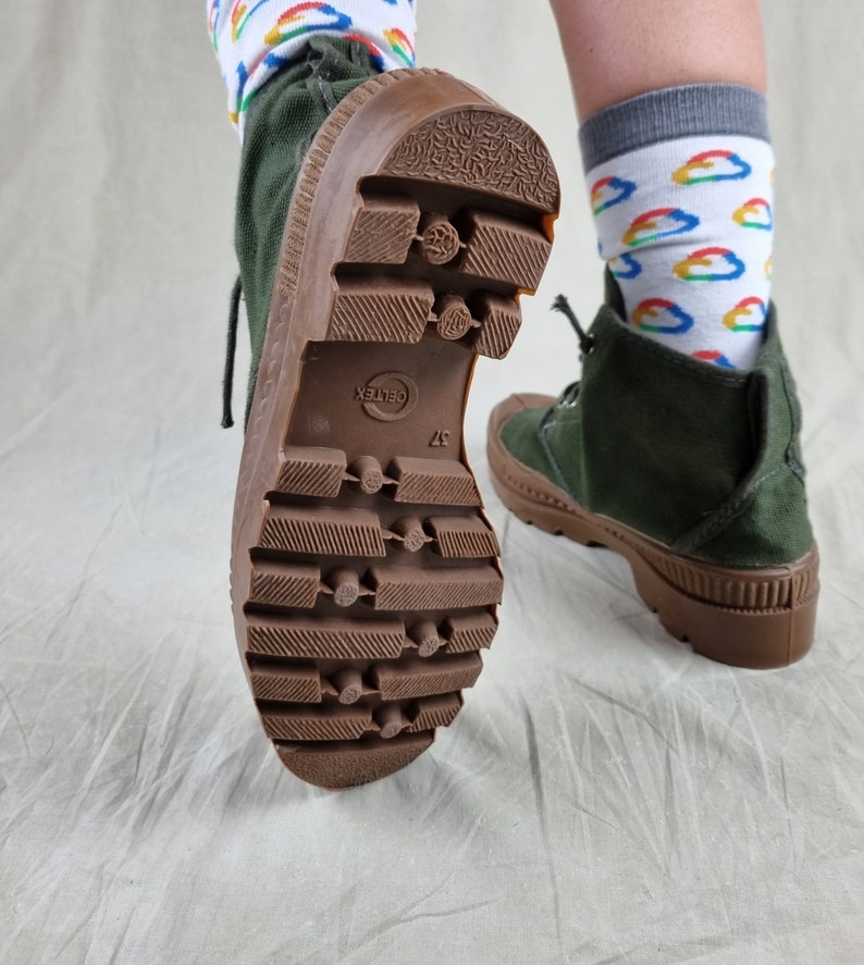 May include: A pair of green canvas boots with brown rubber soles. The boots have a lace-up closure and a textured tread pattern. The text "GELTEX" is visible on the sole of one boot.
