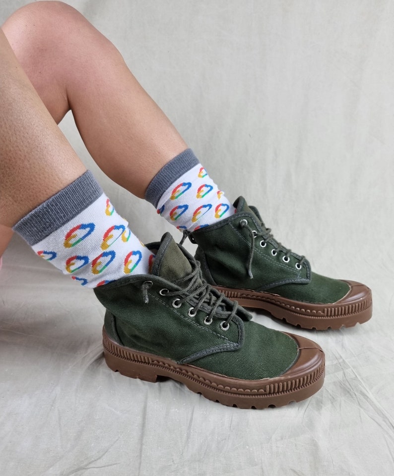 May include: A pair of dark green canvas boots with brown rubber soles. The boots are laced up and have a casual, rugged look. The person wearing the boots is also wearing white socks with colorful rainbow-shaped designs.