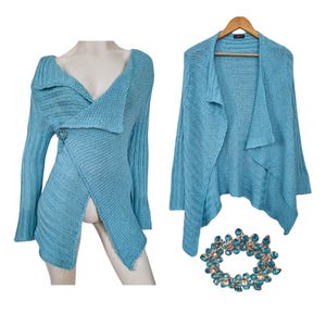 May include: A light blue knitted cardigan with a draped, asymmetrical design. The cardigan has a V-neck and long sleeves.