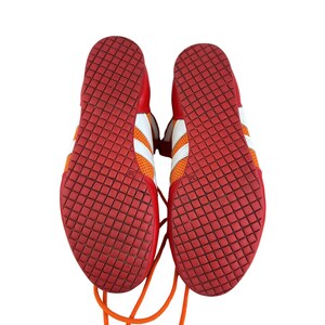 May include: A pair of red and orange athletic shoes with white laces and a white stripe. The shoes have a diamond pattern on the bottom.