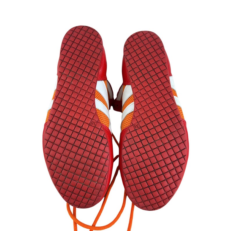 May include: A pair of red and orange athletic shoes with white laces and a white stripe. The shoes have a diamond pattern on the bottom.
