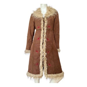 May include: A brown suede coat with a faux fur collar and trim. The coat has a long, flowing silhouette and features red embroidered paisley patterns.