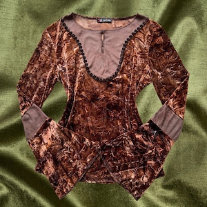 May include: A brown velvet long-sleeve top with a lace trim neckline and bell sleeves. The top has a crinkled texture and a brown underlay.