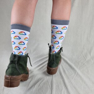 May include: A pair of green ankle boots with brown soles. The person wearing the boots is wearing white socks with a rainbow cloud pattern.